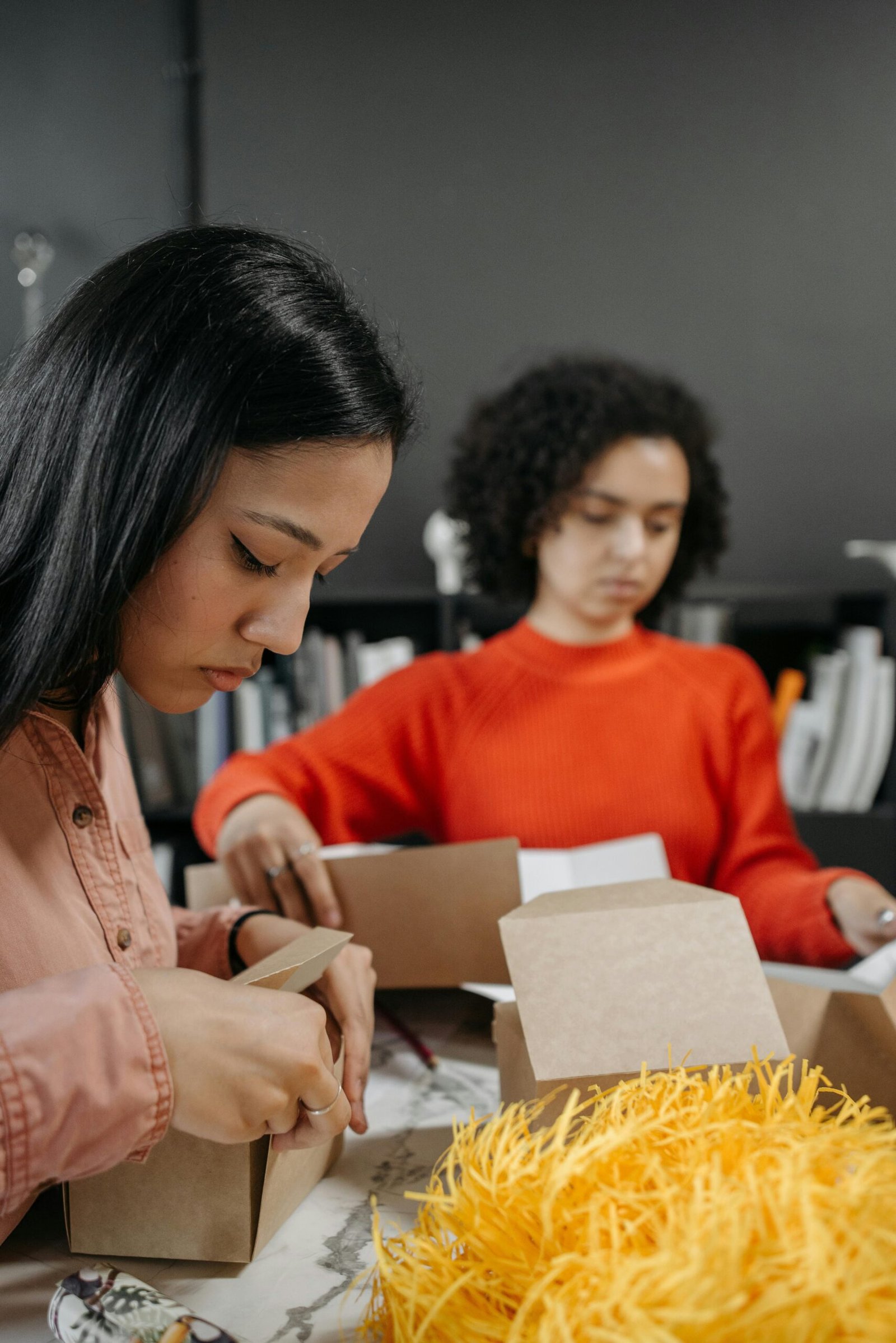 Two women creatively wrapping gifts indoors using eco-friendly materials.