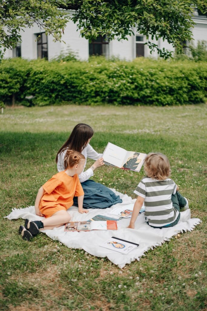 Mother and children enjoy a reading session on a picnic blanket outdoors.